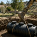 Excavator lowering a black septic tank into a residential pit in San Diego County — Solid State Septic